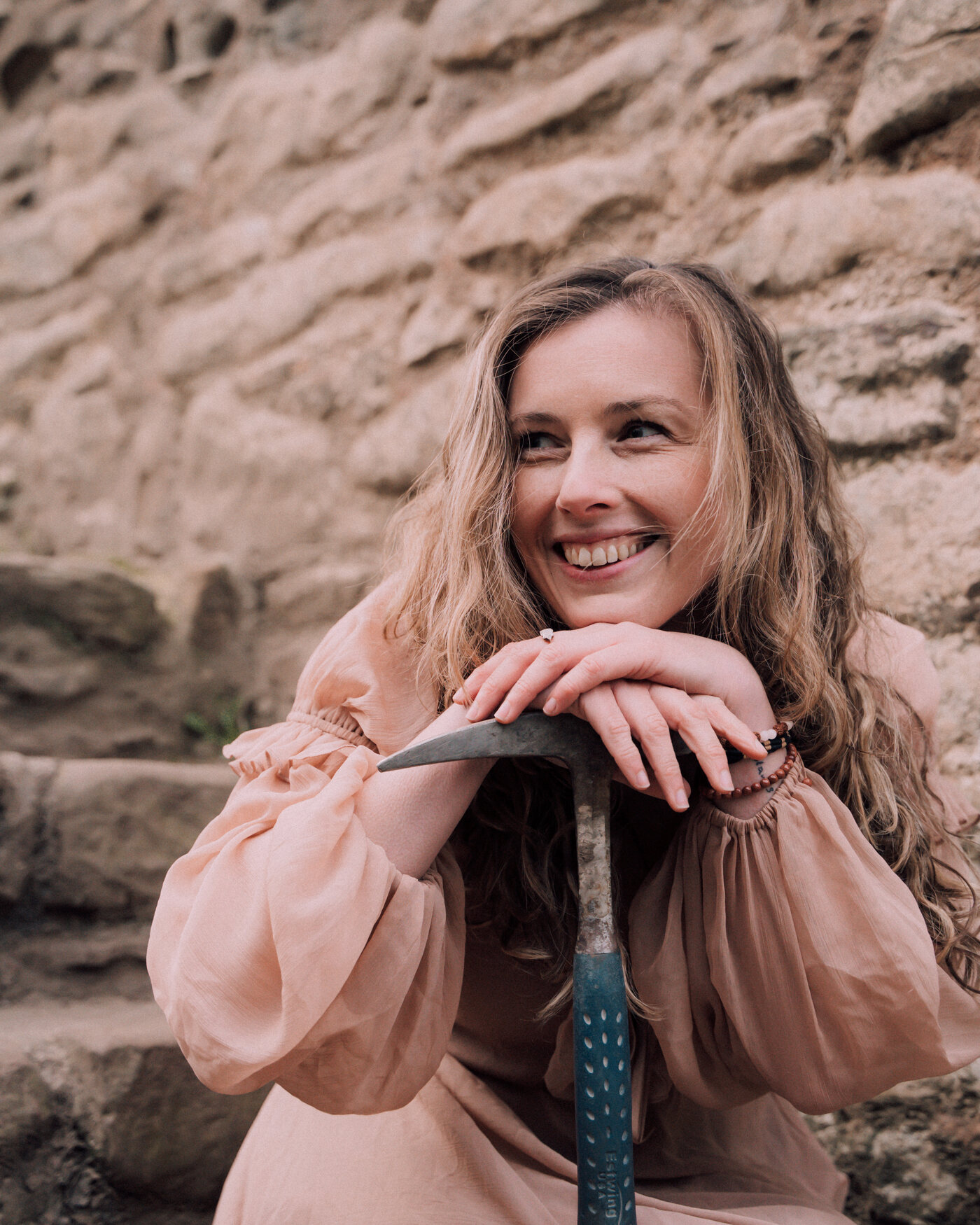 Libby smiling, leaning on a geological hammer against a sandstone wall