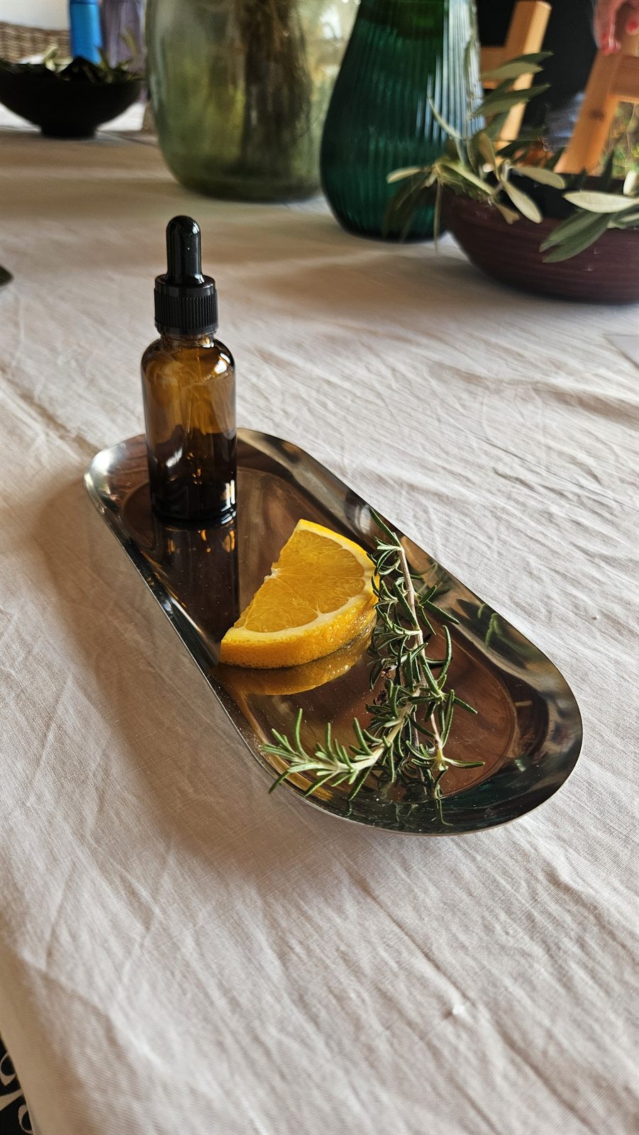 A dropper bottle of essential oil on a tray with a slice of orange and a sprig of rosemary