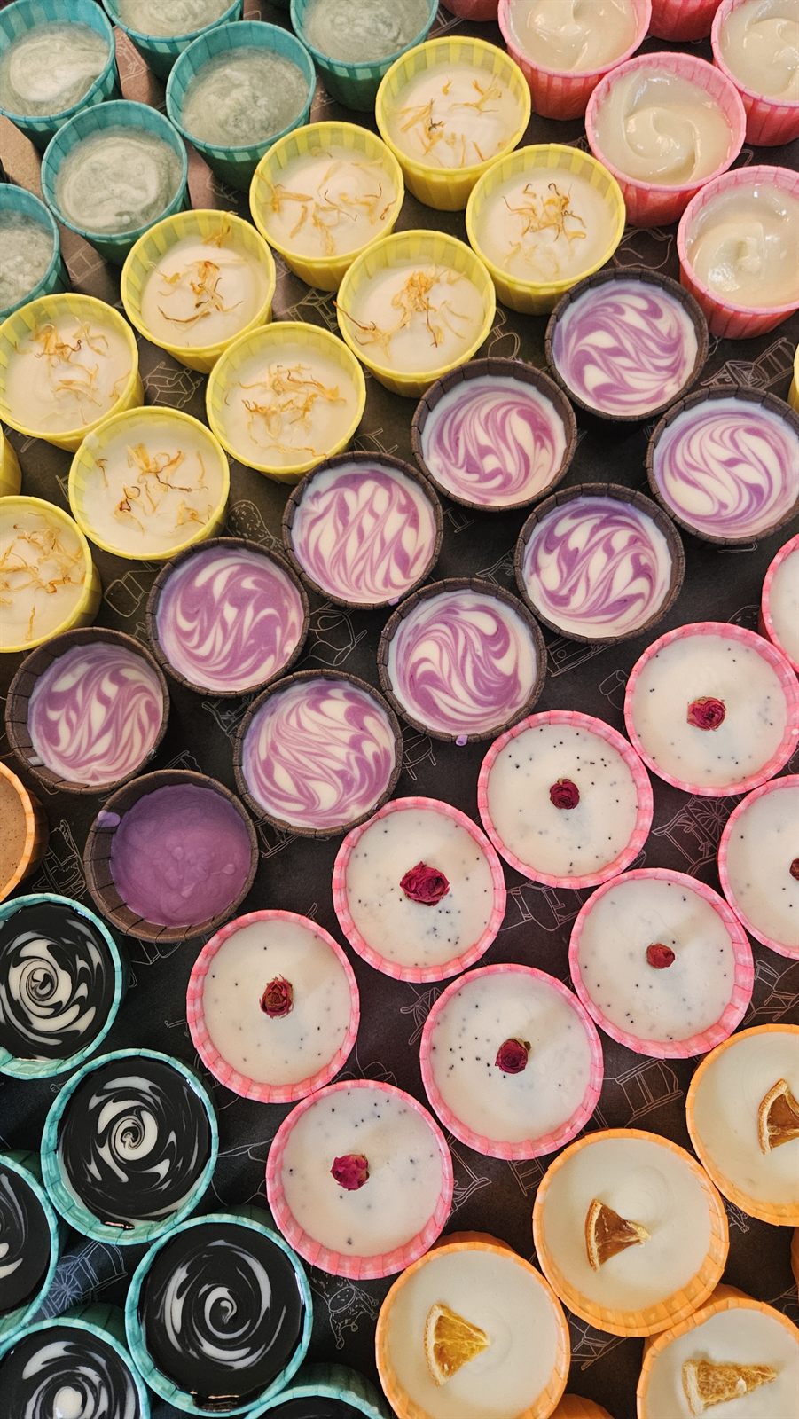 Rows of handmade soaps setting in colourful moulds, topped with petals, rosebuds and dried orange