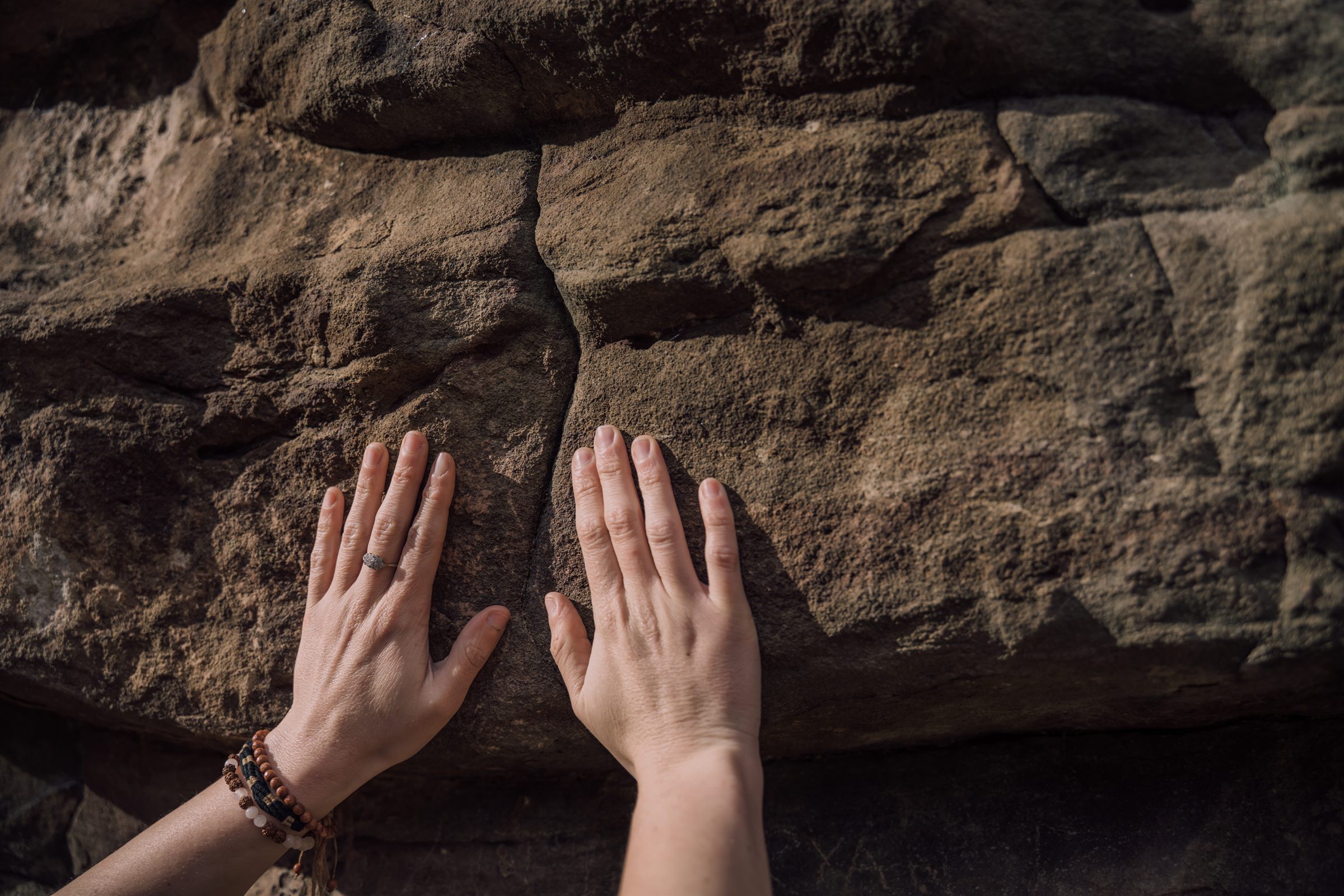 Two hands pressed flat against a weathered red sandstone wall