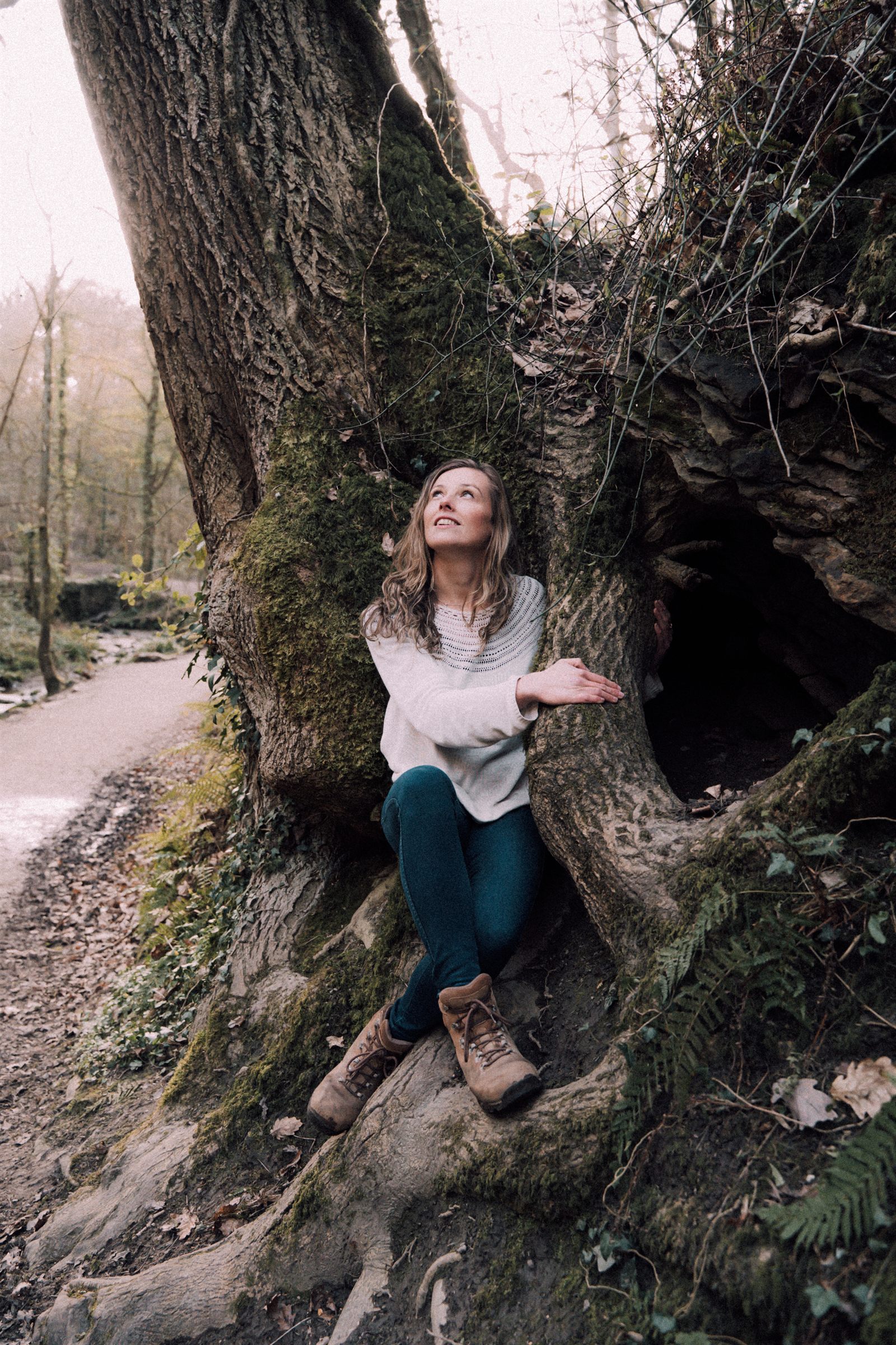 Libby sitting among the mossy roots of an old tree, looking up