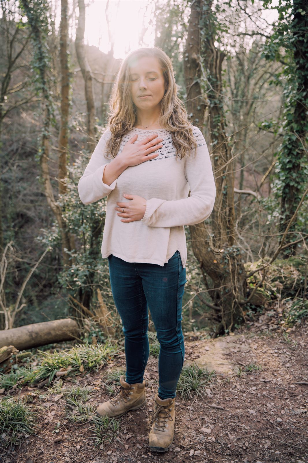 Libby standing in sunlit woodland, eyes closed, one hand on her heart